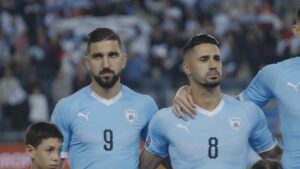 Two men in light blue soccer jerseys stand on the field.