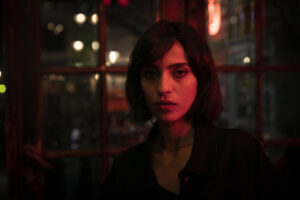 A woman with short dark hair stands in a room washed with red light