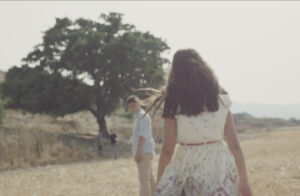 A young boy and girl walk towards a tree in a field