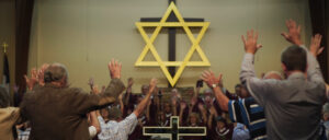 A group of people pray with their arms up. Above them there is a large Star of David.