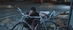 A man squats next to a locked bicycle. He is also on the phone.